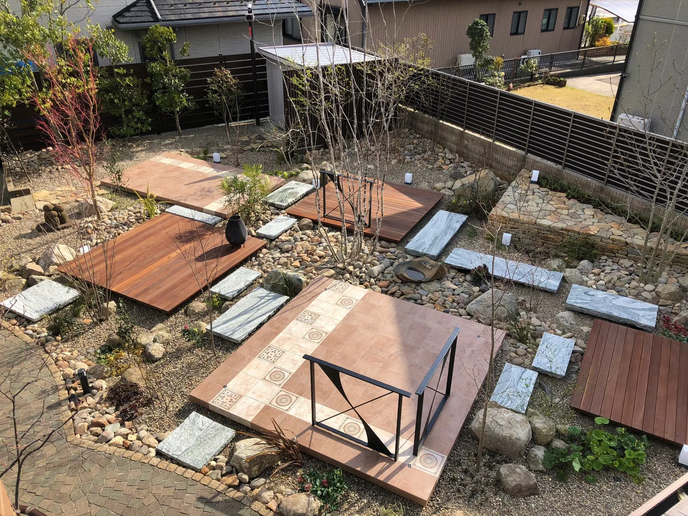 庭石や植栽の間へ点在させた複数のウリンデッキを周囲の庭や建物とともに見る全景
