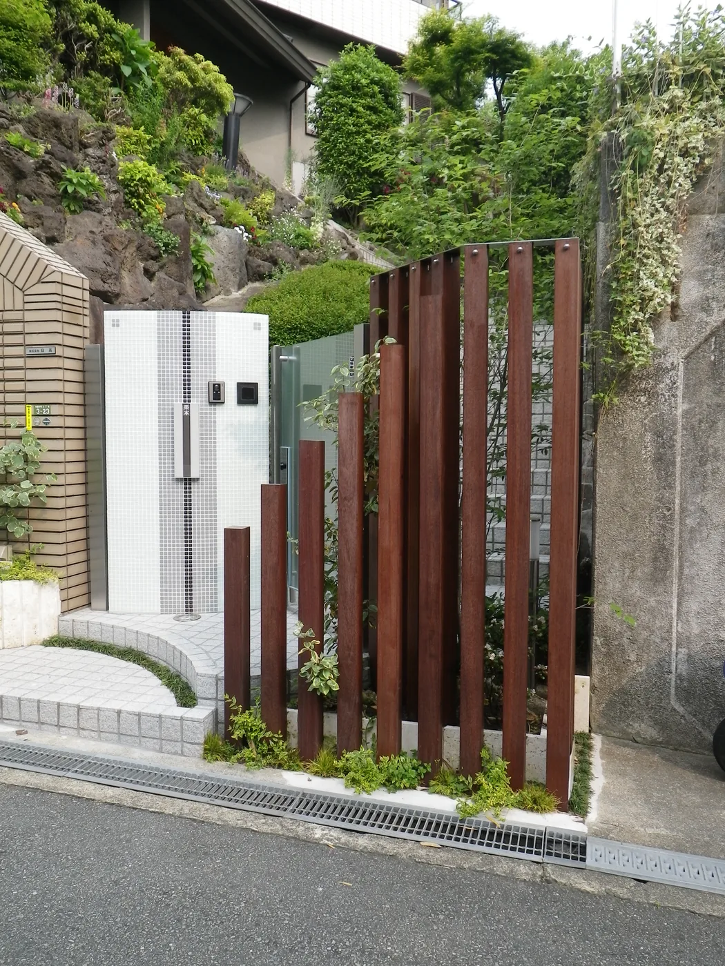 完全に閉じる板塀ではなく、格子の高さと間隔を変えて入口と庭の奥を緩やかに区切っています
