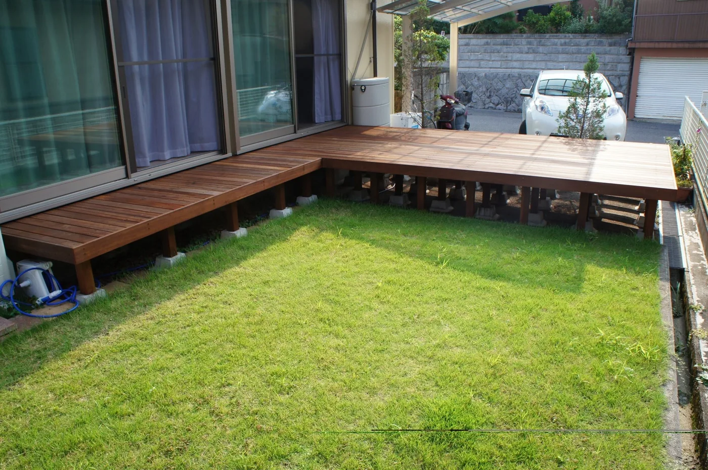 芝生の二辺を囲むL字型ウリンデッキと階段を周囲の庭や建物とともに見る全景