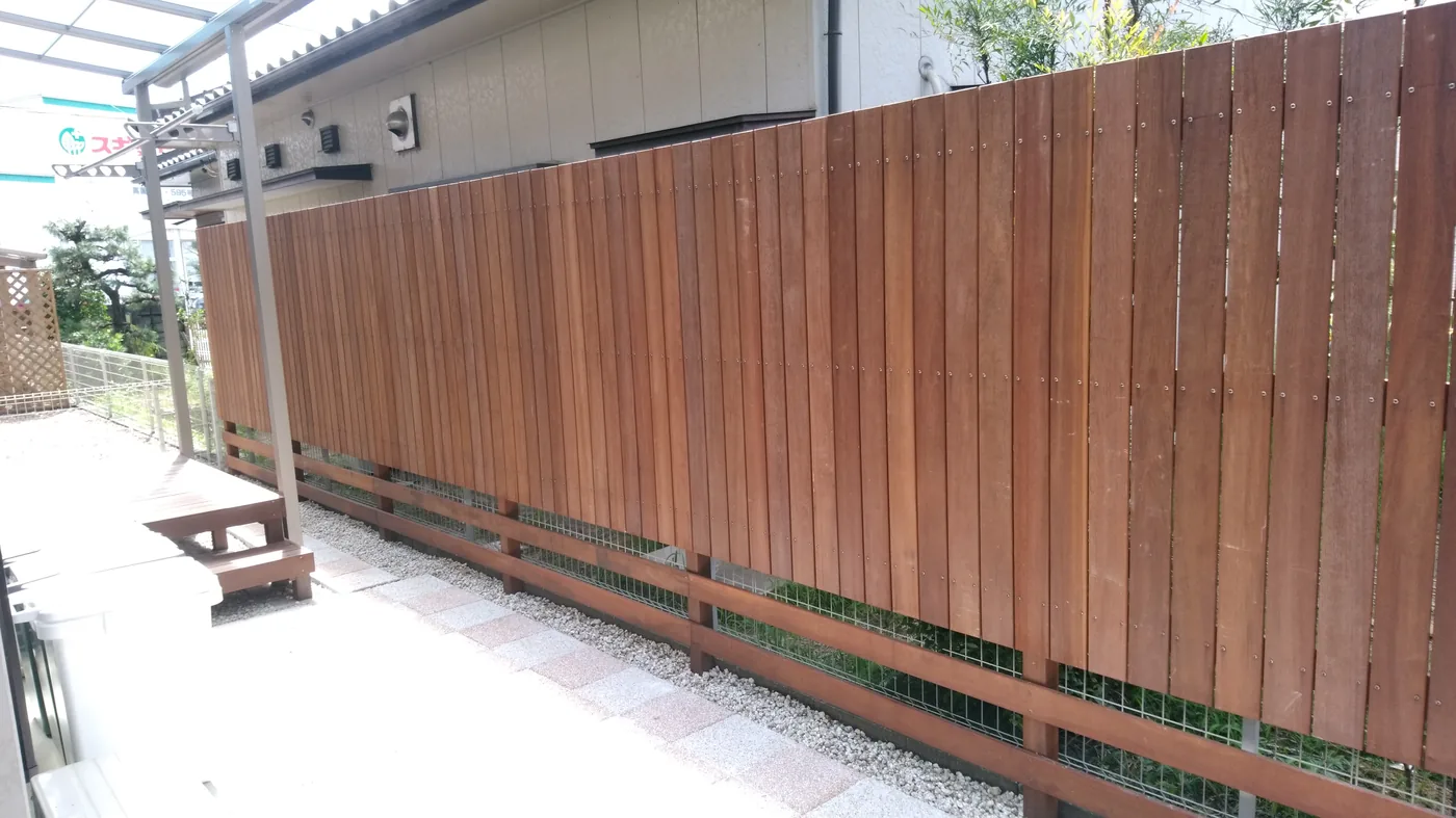 敷地境界へ設けた背の高いウリン縦格子フェンスと周囲の庭・建物を一緒に見る全景