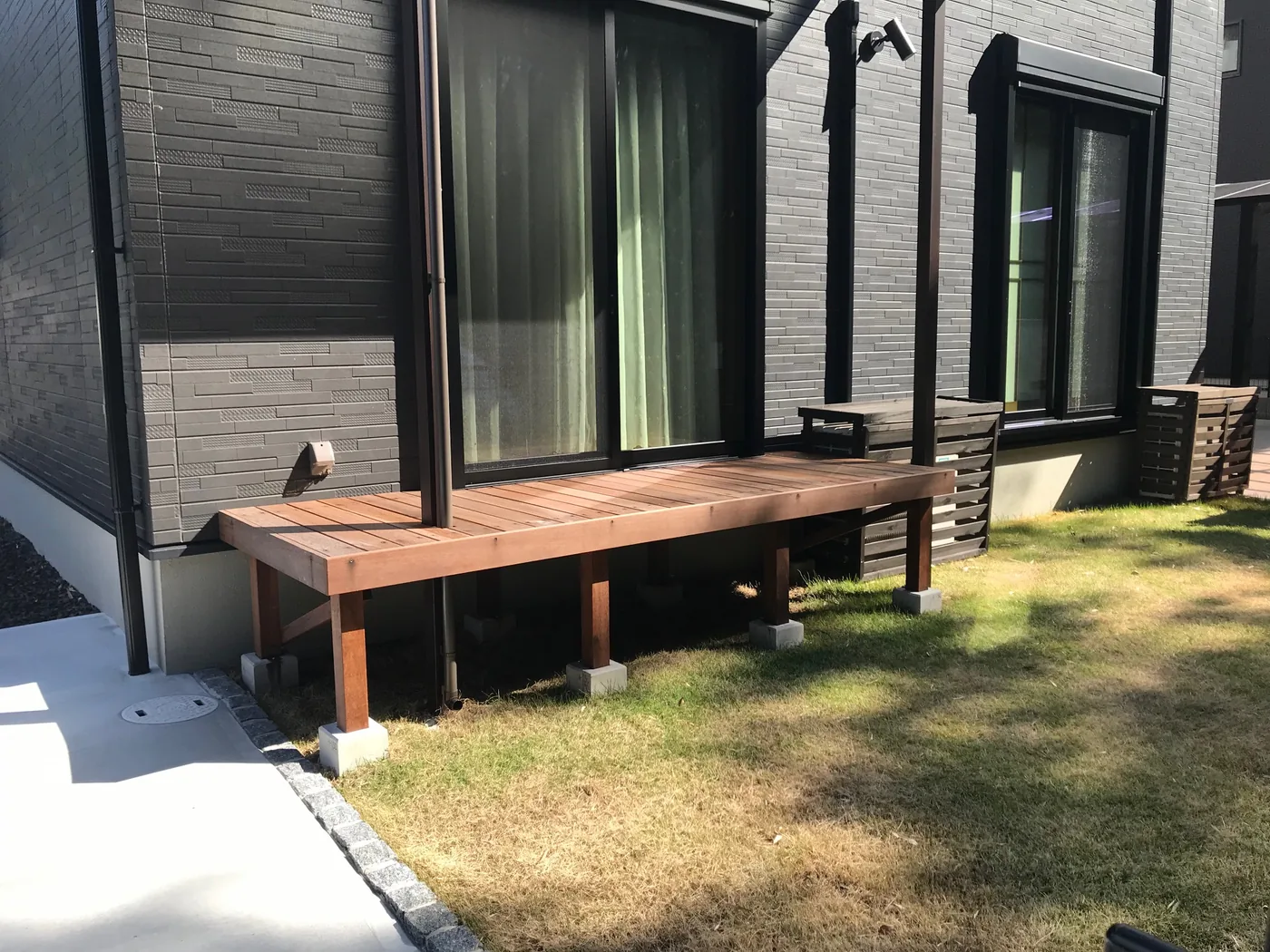 黒い外壁と芝生の庭に沿うウリン縁側デッキ