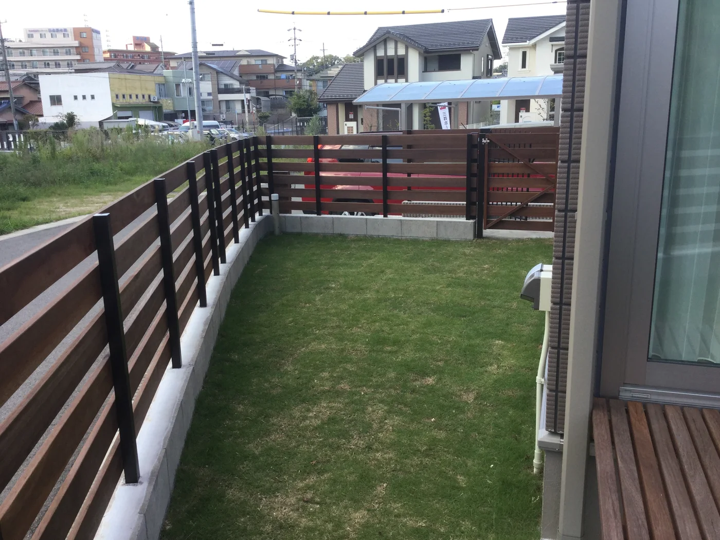 建物脇から見渡す芝生のドッグランと横板フェンス