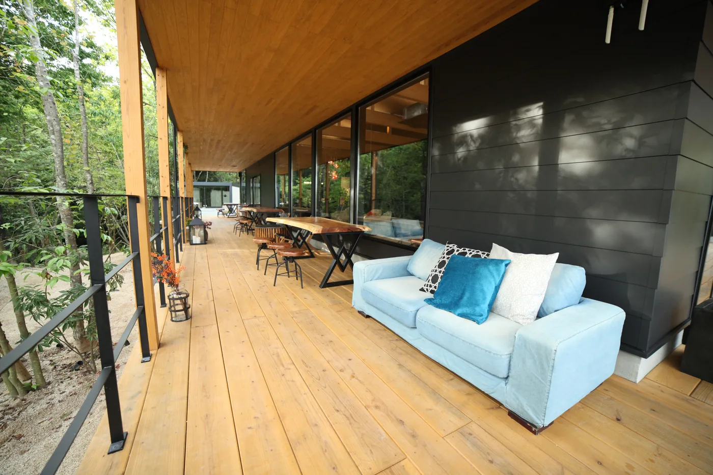 黒い外壁に沿う屋根付きの屋外ラウンジデッキ