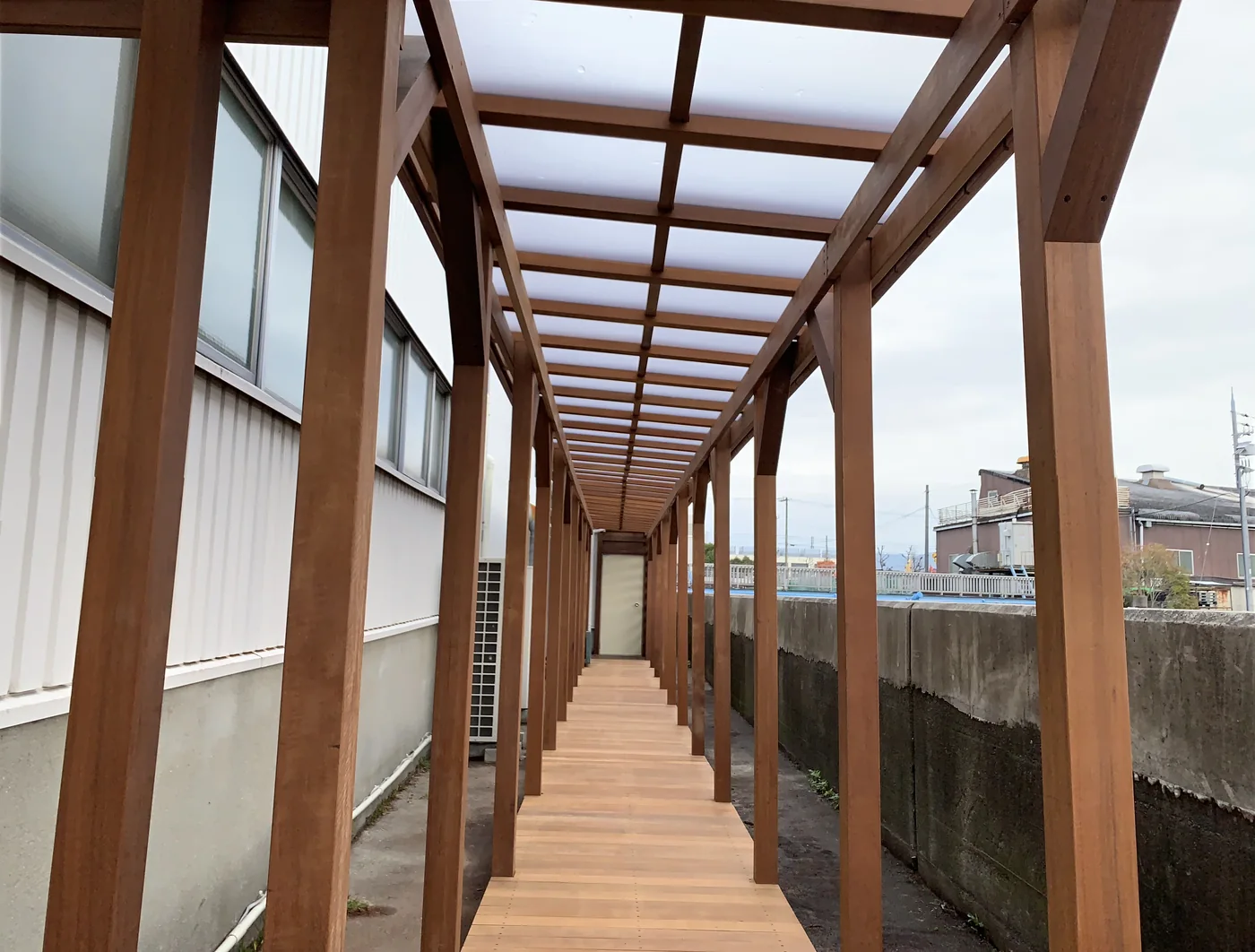 長い木床と屋根状フレームが続く屋外通路の全景
