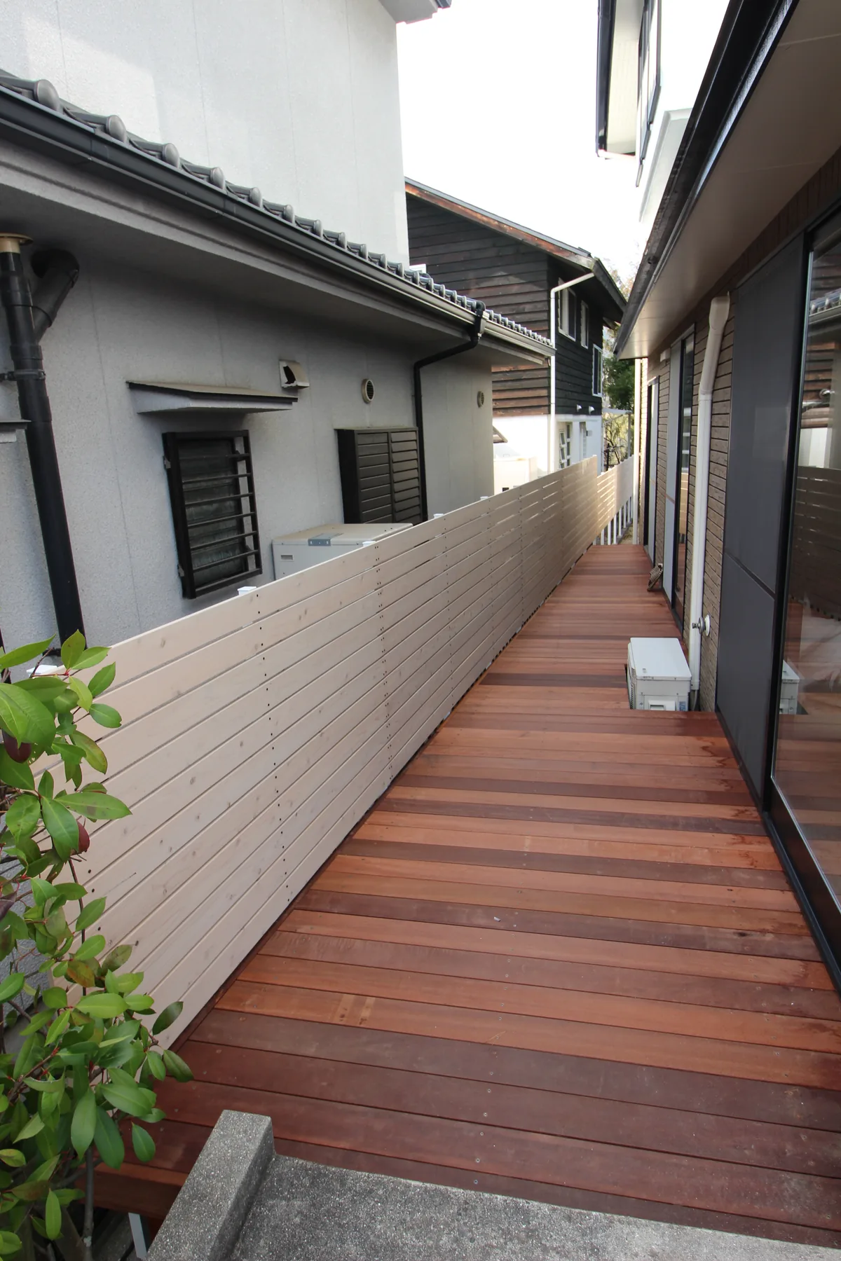建物と塀の間に伸びる細長いウリン通路デッキ