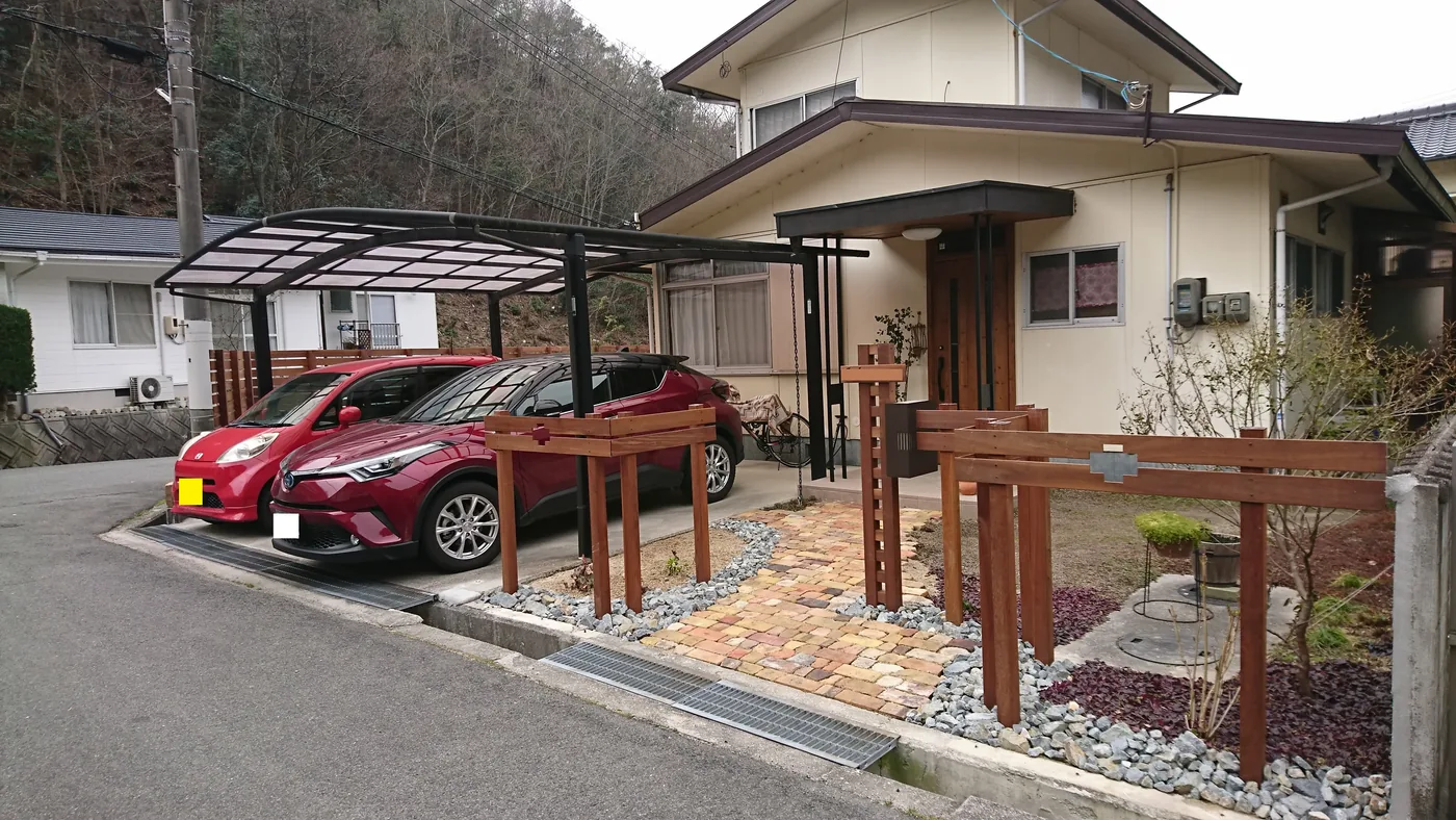 門まわりの木柱と小さなデッキを含む庭の全景