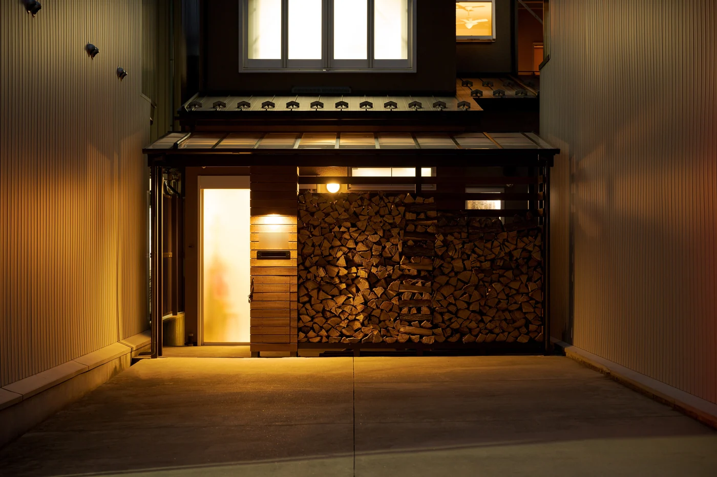 照明を点けた夜の玄関と薪置き場