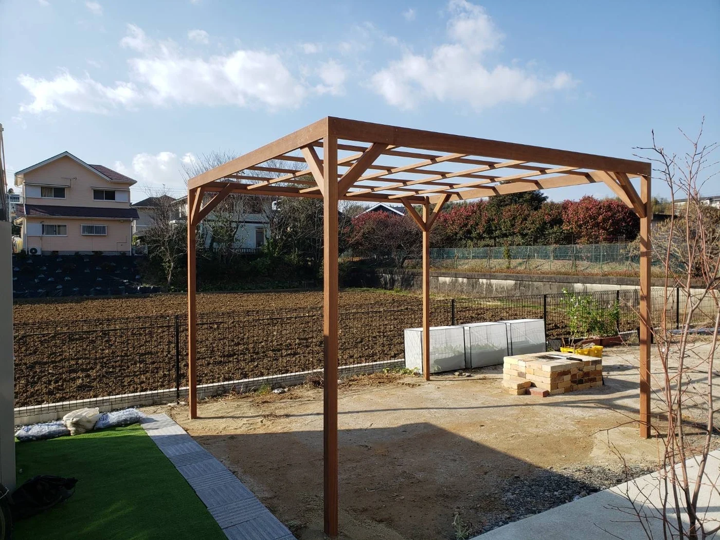 側面を開いた木製フレームと、畑へ抜ける庭の全景です